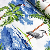 Tropical patterned fabric with heron & toucan birds, palm leaves, and blue waves on a white background.