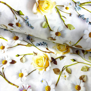 White cotton poplin fabric printed with a floral pattern featuring yellow roses, white daisies with yellow centers, and small blue flowers with green stems.
