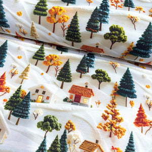 Upholstery fabric with winter village pattern featuring trees, houses, and colourful leaves on a white background.