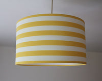 Striped lampshade with yellow and white stripes on a plain background.