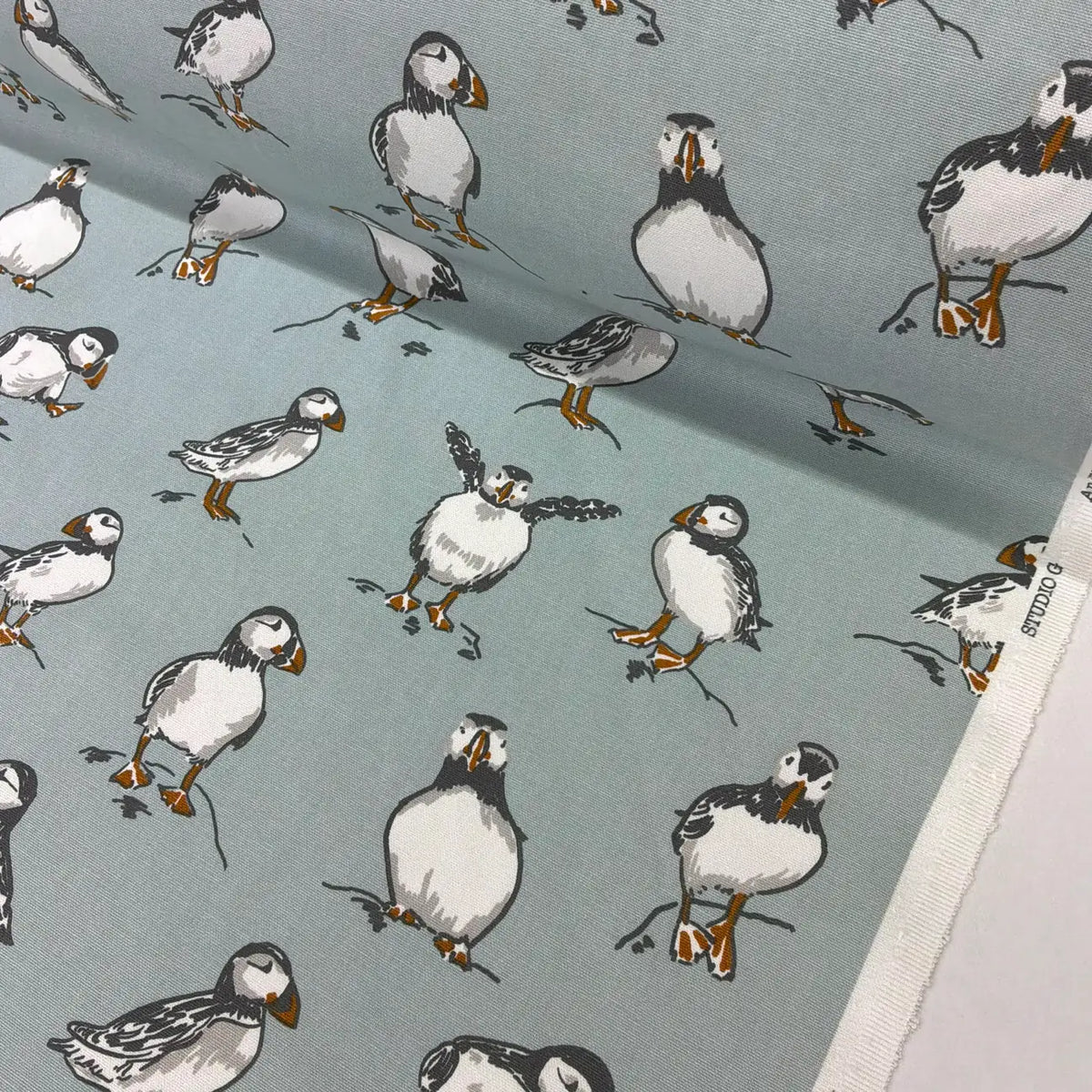 A close-up of fabric featuring a repeating print of puffins on a muted blue-gray background. 