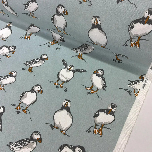 A close-up of fabric featuring a repeating print of puffins on a muted blue-gray background. 