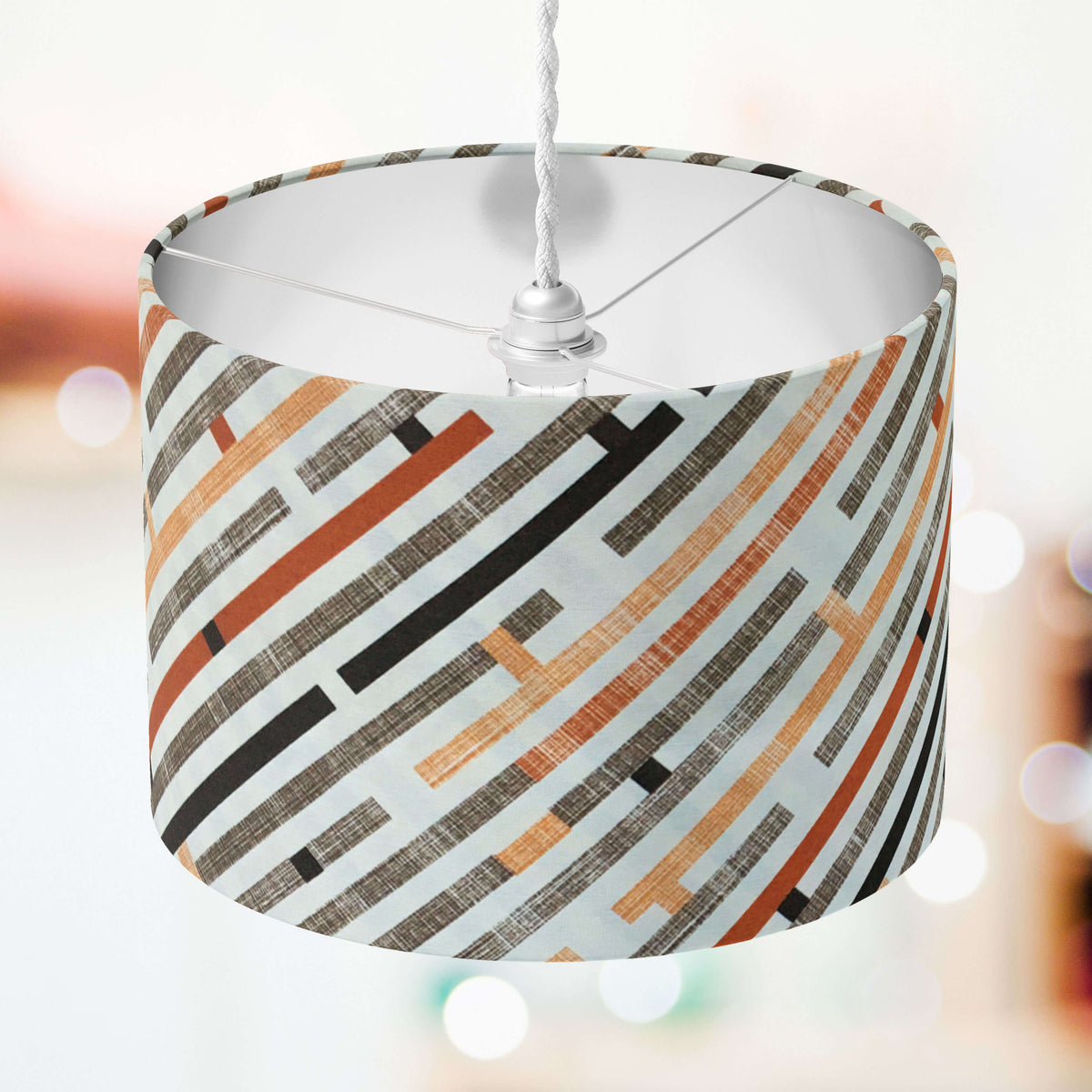 Maze striped patterned lampshade in orange, terracotta, brown, black and white with a blurred background.