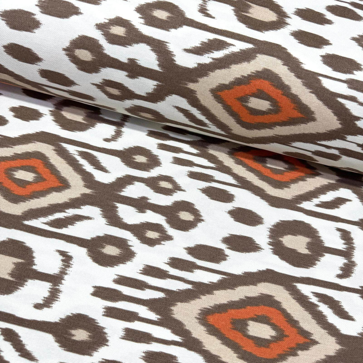 Ikat patterned upholstery curtain fabric with geometric design in brown, orange, and beige on a white background.