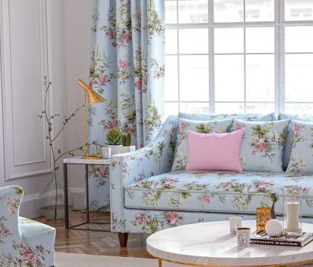 A sofa covered with a blue, pink and green floral upholstery fabric and a curtain made with the same material in a living room. 
