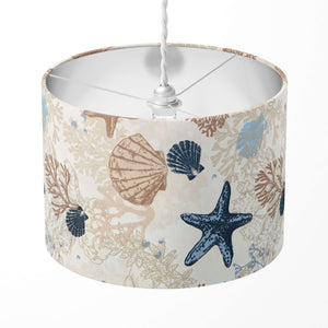 A cylindrical beige lampshade with a nautical pattern featuring seashells and starfish in shades of blue.