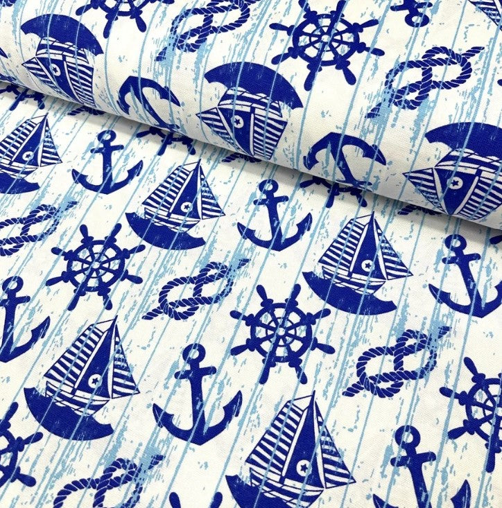 Rustic upholstery fabric printed with royal blue sailboats anchors rope knots ship wheels on a white background.