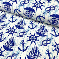 Rustic upholstery fabric printed with royal blue sailboats anchors rope knots ship wheels on a white background.
