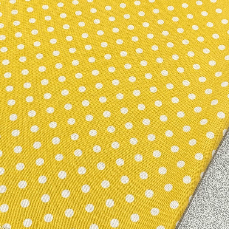 Yellow polka dot cotton canvas upholstery fabric with white spots on it.