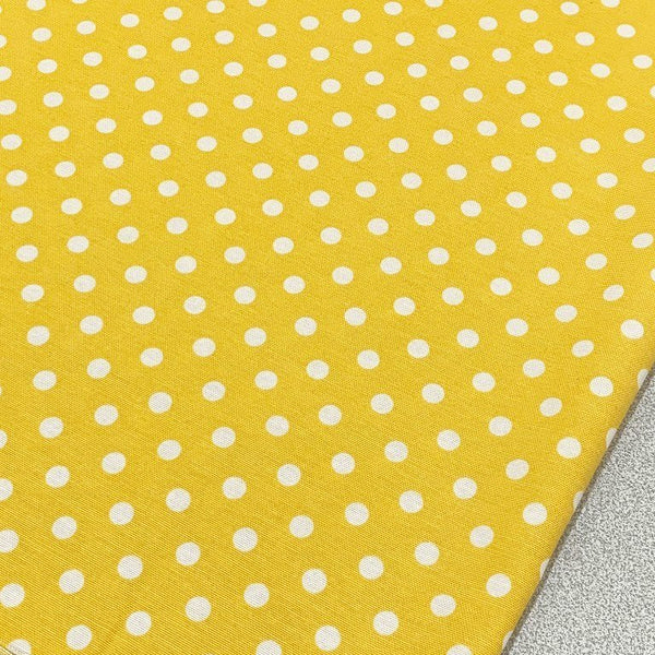 Yellow polka dot cotton canvas upholstery fabric with white spots on it.