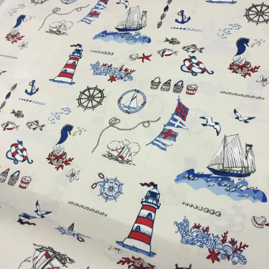 A fabric with a nautical theme, featuring various blue ocean and lighthouse patterns, suitable for decor and upholstery.